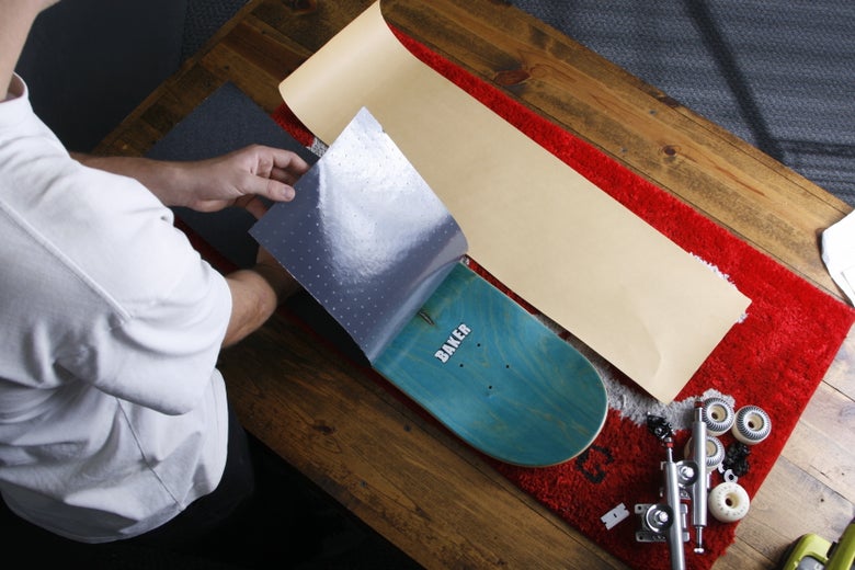 A person places griptape on a skateboard deck.