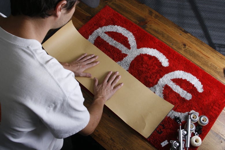 A person uses the backing of the griptape sheet to flatten and adhere the griptape on a skate deck.