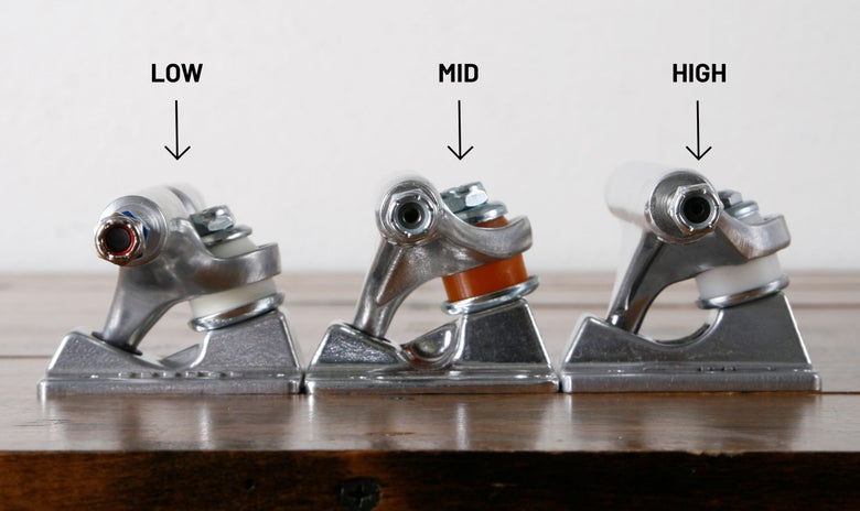 Low, mid, and high skateboard trucks sit next to each other on a table with their profile height labeled. 