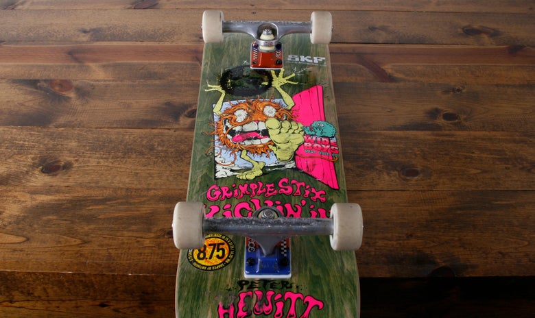 A complete skateboard with newly installed trucks and wheels sit on a wood table. 