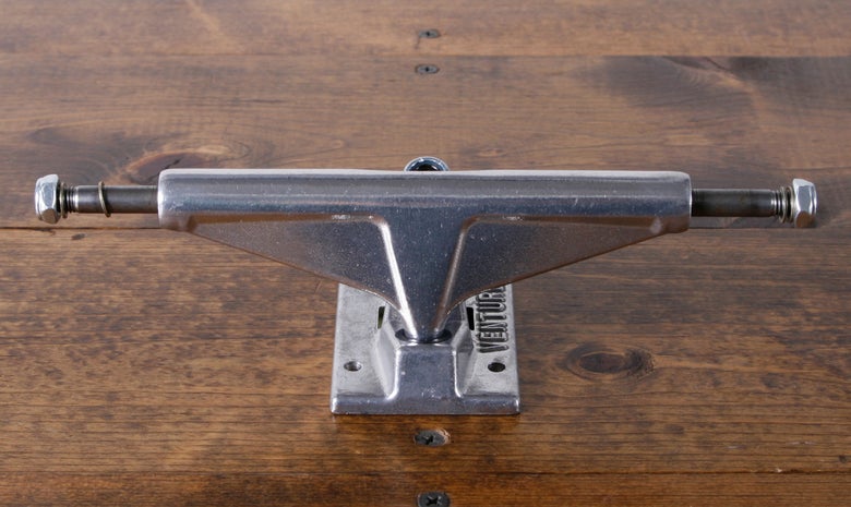 A Venture OG Polished High skateboard truck sits on a wood table. 