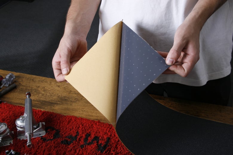 A person peels the protective backing off of skateboard griptape. 